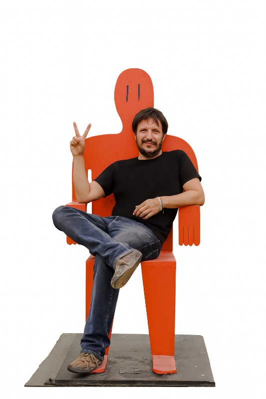 Pablo Zeta sentado sobre una escultura de un Hombre Rojo